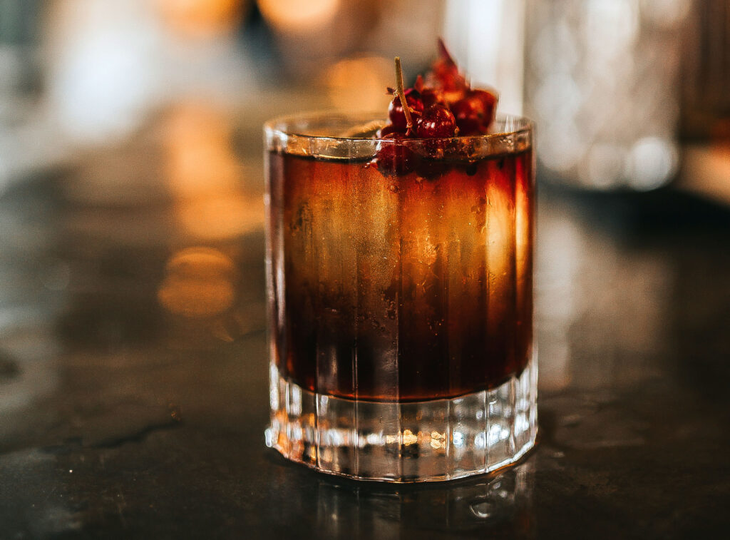 A close up shot of classic Old Fashioned cocktail served with a cube of ice and garnished with cranberries. Concept of bourbon whisky, spirits and alcohol.